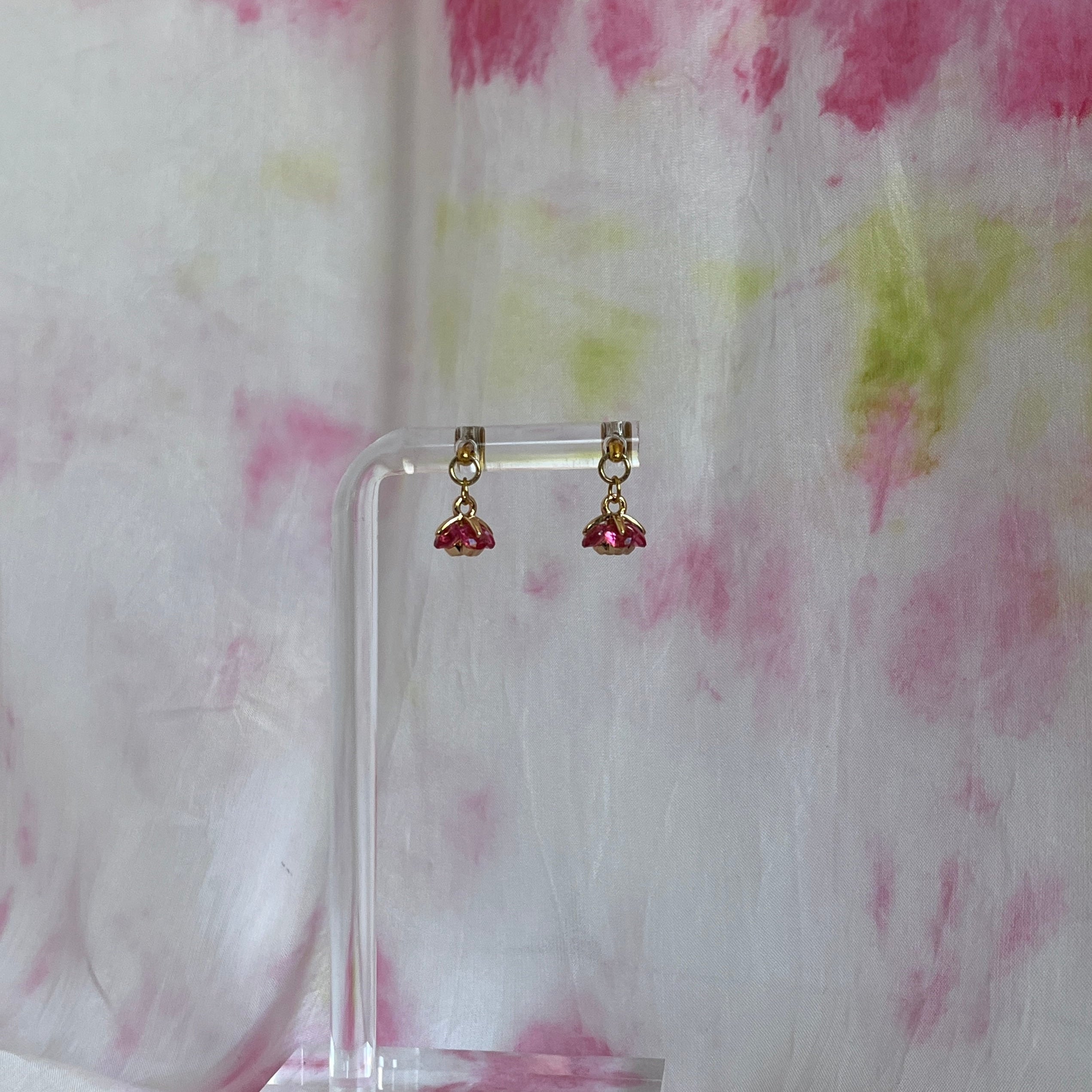 Pair of earrings on a clear stand against a floral fabric background