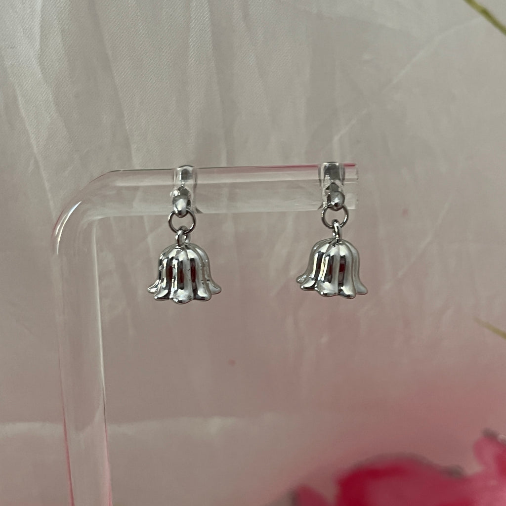 Silver bell-shaped earrings on a clear stand with a light background