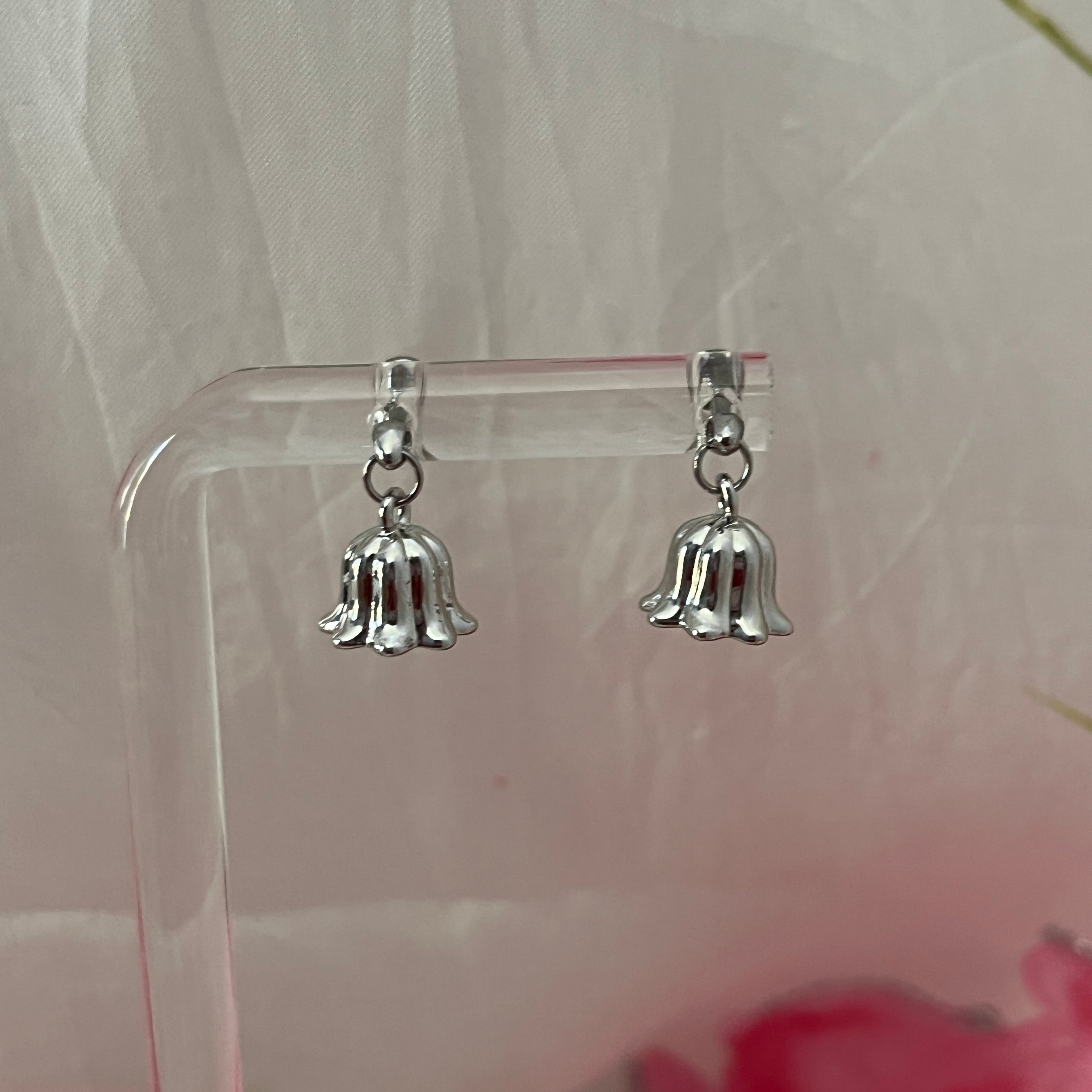 Silver bell-shaped earrings on a clear stand with a light background